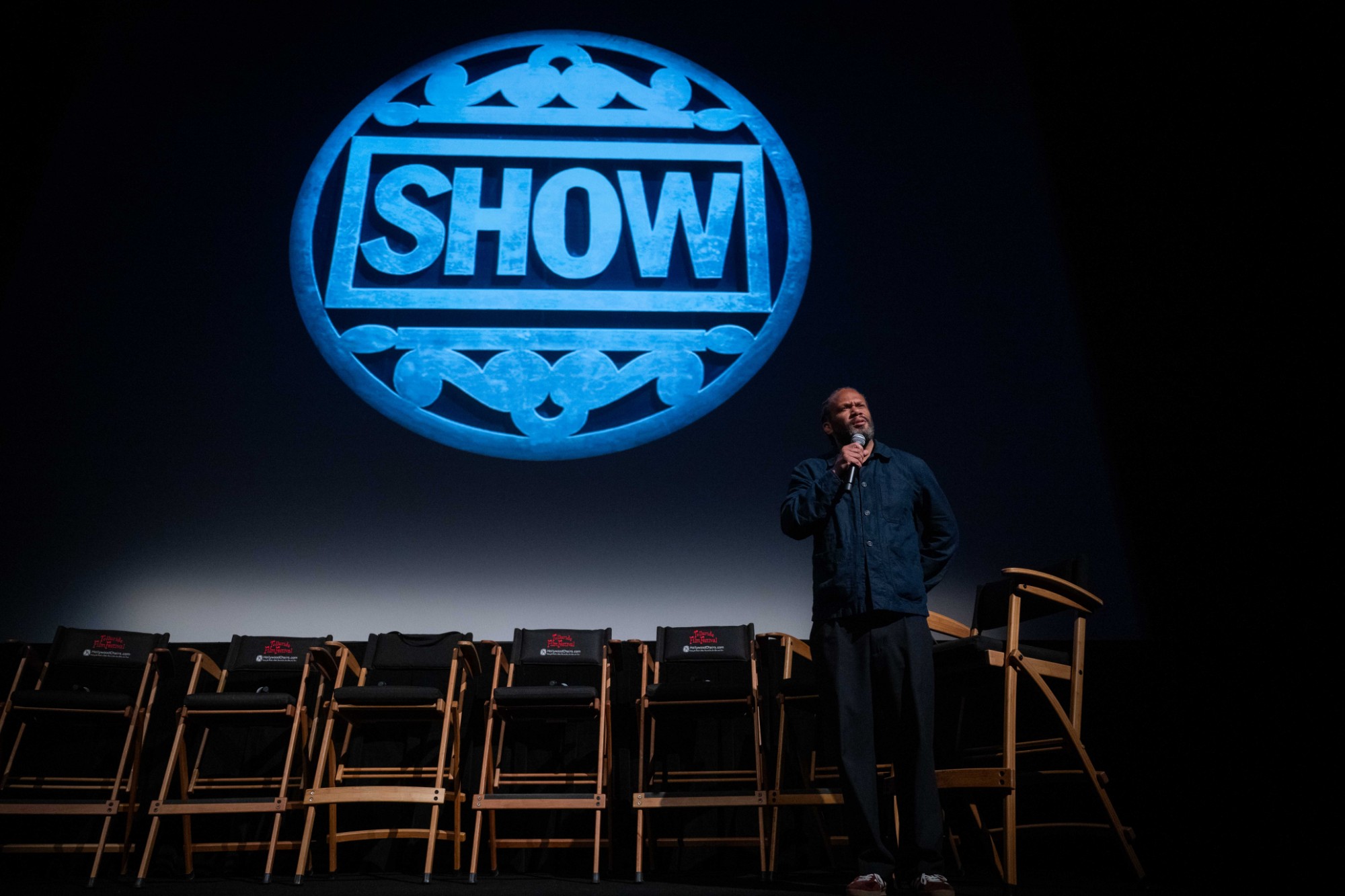 Franklin Leonard alone on a stage beside a row of empty chairs, beneath the Telluride Film Festival SHOW logo